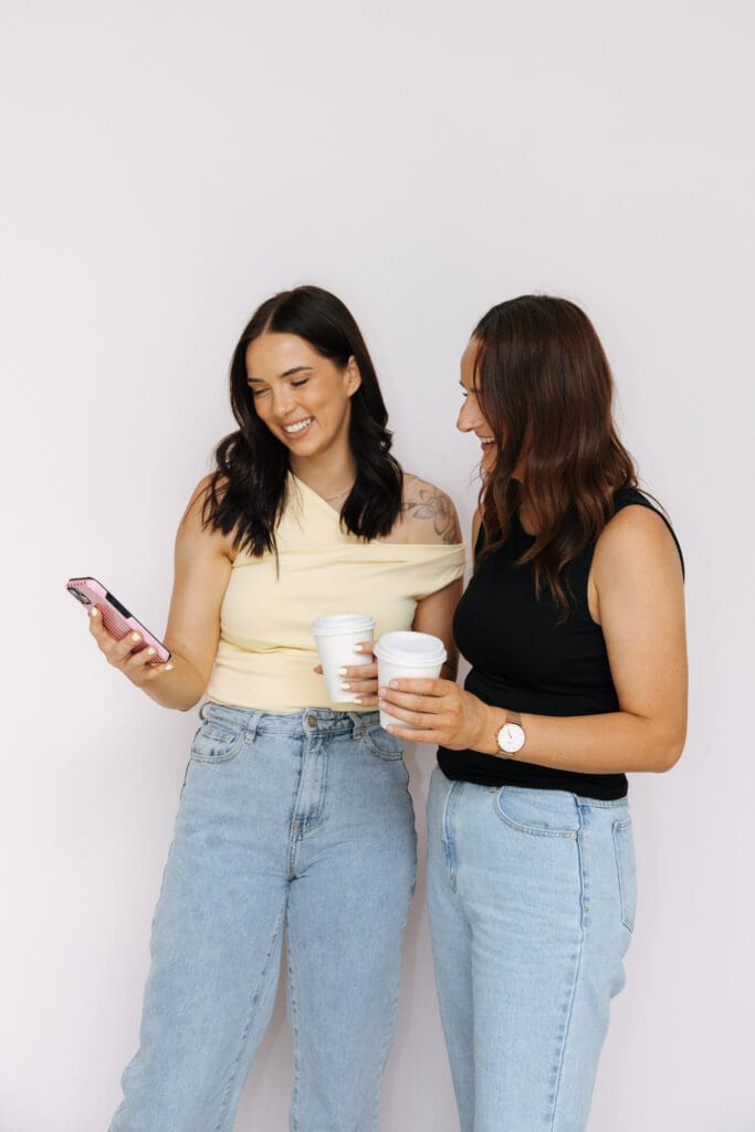 Aimee and Ash from Coja Creative at Studio Sohl in Warrnambool Victoria. in front of the studios pink backdrop. Both looking at a phone.